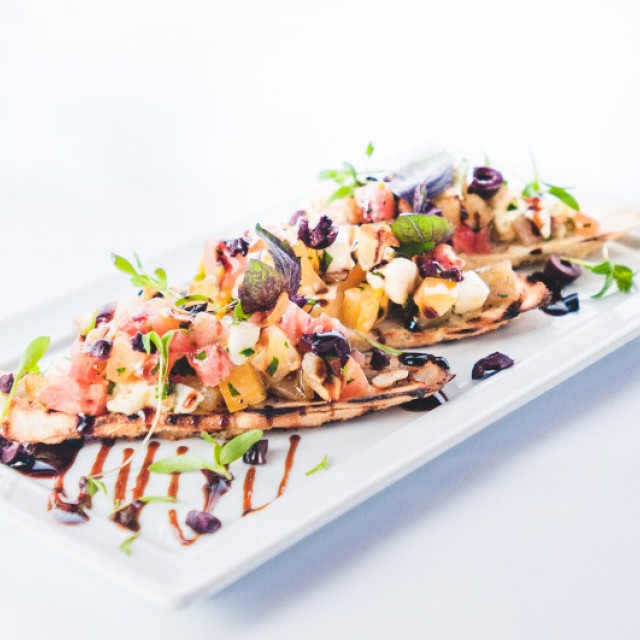 Food Photo of Bruschetta on two long pieces of grilled baguette bread with Tri color tomatoes, micro greens and balsamic drizzle