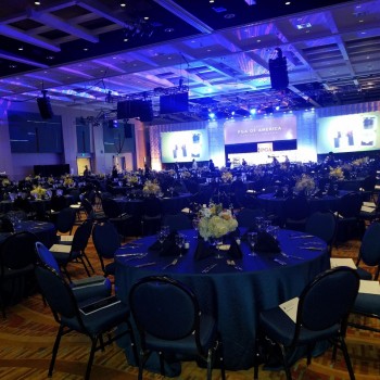 Photo of a three screen display hung from the ceiling against the wall in the front of the building with hanging event logo displays in between each screen. Screens display the Palm Beach County Mayor's Breakfast event.